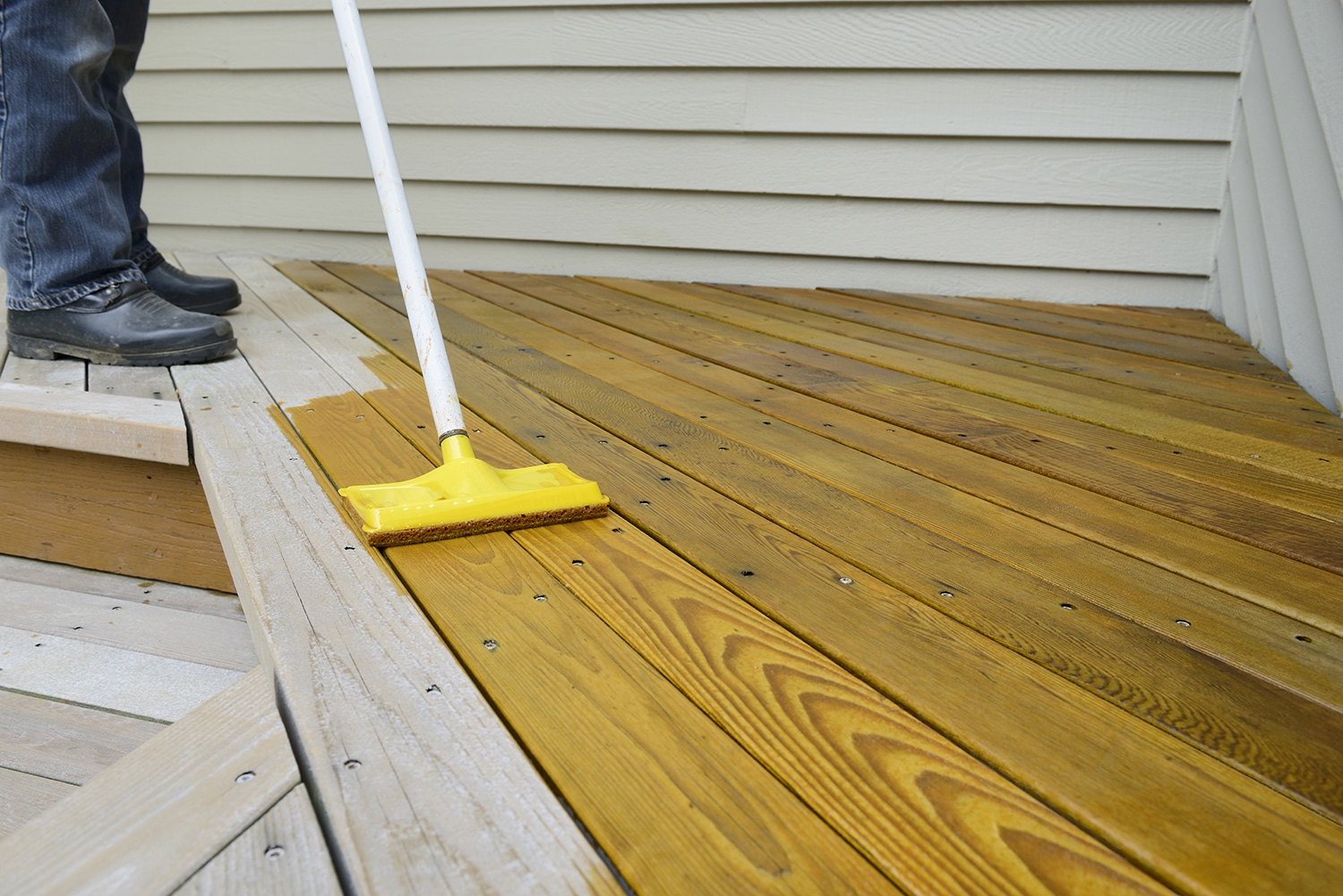 Painter using sponge applicator to apply stain to deck.
